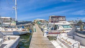Un puerto deportivo con barcos amarrados a lo largo de un muelle de madera, que conduce a un edificio con zona cubierta.