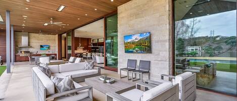 A modern living room with a large TV, comfortable seating, and a view of the outdoors.