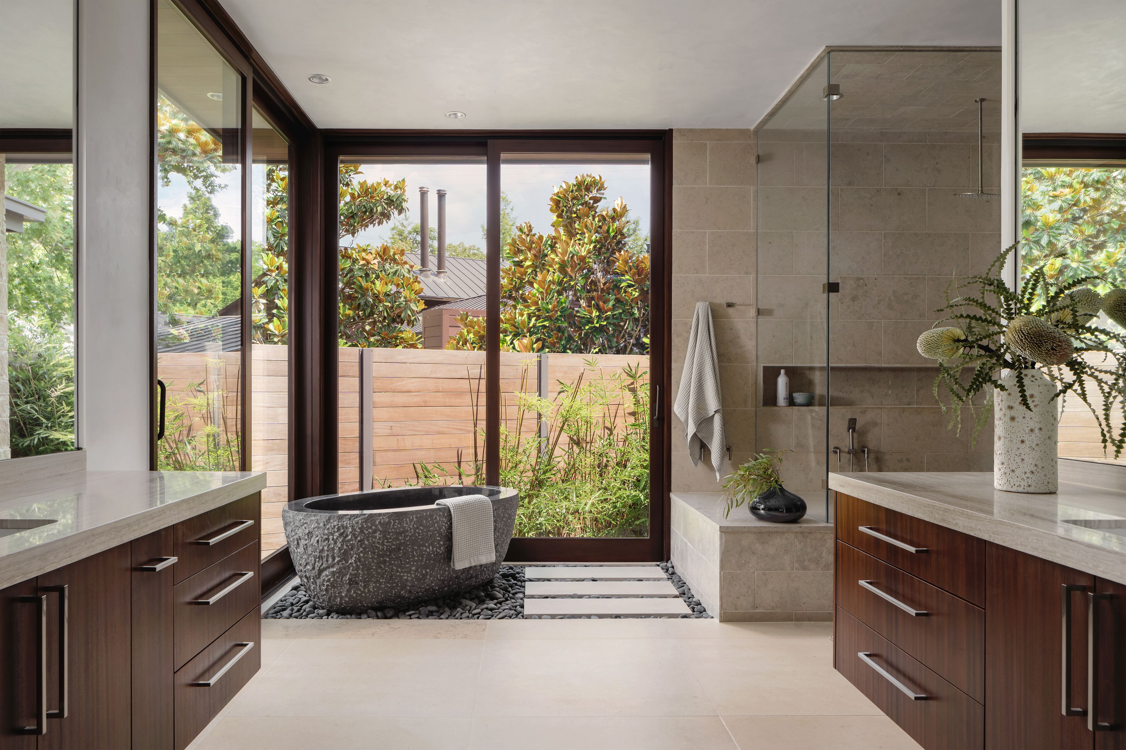 Un baño moderno con una bañera independiente, cabina de ducha con mampara de vidrio y vista a un jardín.