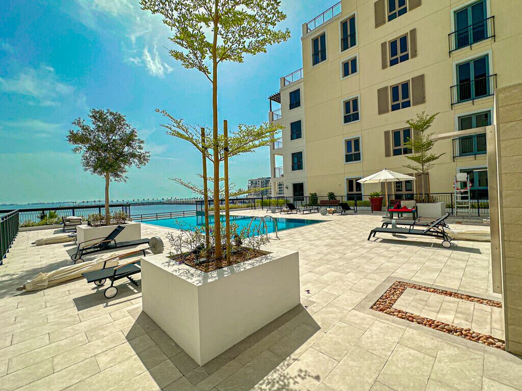 A rooftop pool area with lounge chairs, a small tree, and a view of the sea.