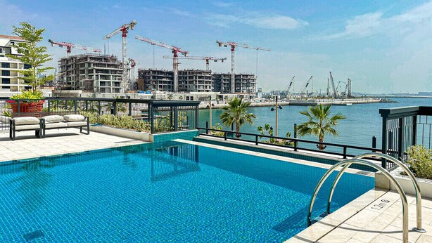 A swimming pool with a view of a construction site and a body of water. - HiGuests - La Rive 2 (Dubai)