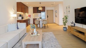 A modern apartment with a living room, dining area, kitchen, and a TV. - HiGuests - La Rive 2 (Dubai)