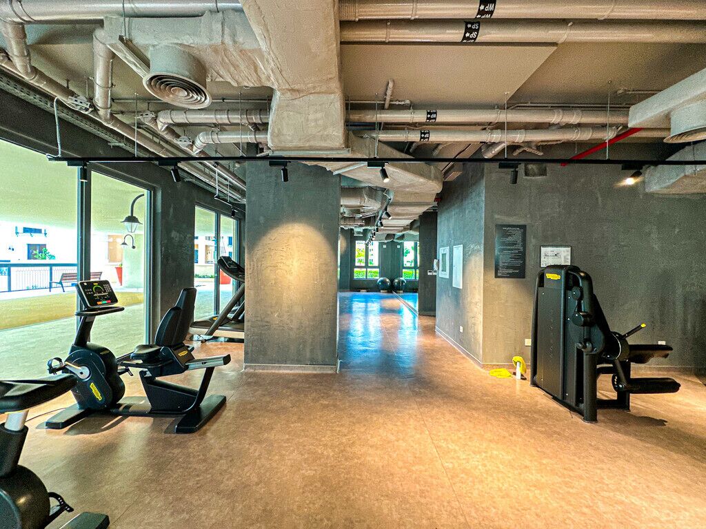 Ett gym med träningsutrustning, ett betonggolv och stora fönster.