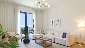 A modern living room with a sofa set, a coffee table, and a dining table. There is a balcony with a view of the sea. - HiGuests - La Rive 2 (Dubai)