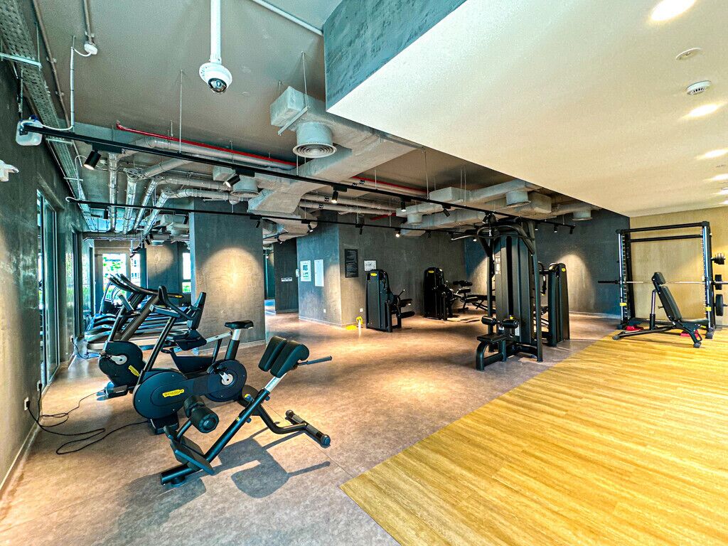 Une salle de sport moderne équipée de machines de cardio, d’appareils de musculation et dotée d’un plancher en bois.