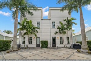 A two-story building with a symmetrical facade, palm trees, and a paved courtyard.