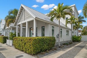 Une maison blanche avec un toit à pignon, une véranda et une haie bien entretenue.
