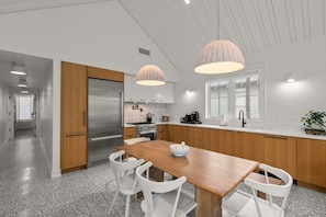 Eine moderne Küche mit einem Holzespeisetisch, weißen Stühlen, Edelstahlgeräten und Pendelleuchten.