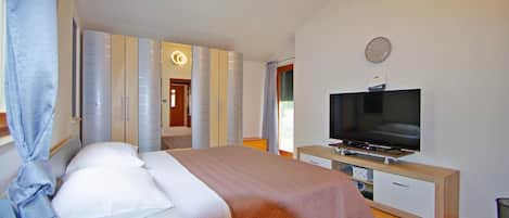 A bedroom with a bed, a television, a wardrobe, and a clock on the wall.