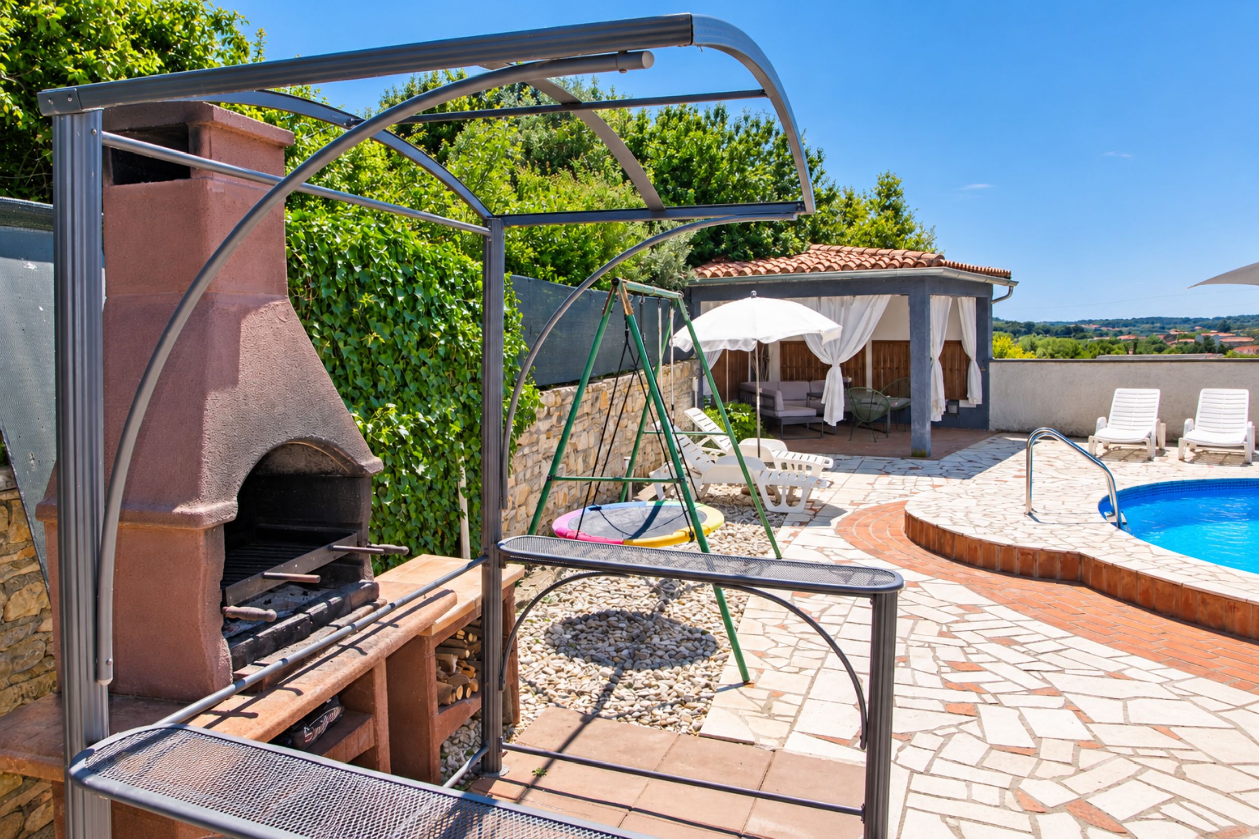 Un jardin avec un barbecue, une balançoire, une piscine et un espace salon abrité.