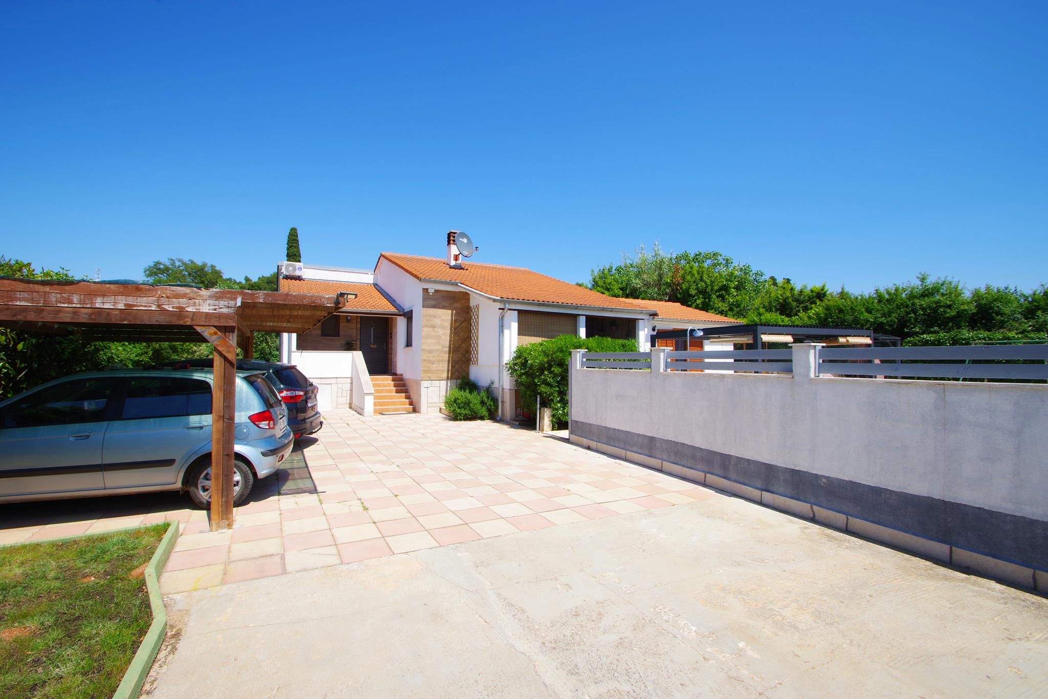 Une propriété résidentielle avec une allée pavée, une voiture garée sur le côté gauche, une pergola en bois et une maison moderne avec un toit en tuiles.