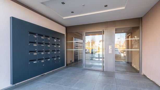 Un couloir moderne, avec une rangée de casiers sur le côté gauche et une porte d’entrée en verre sur le côté droit.