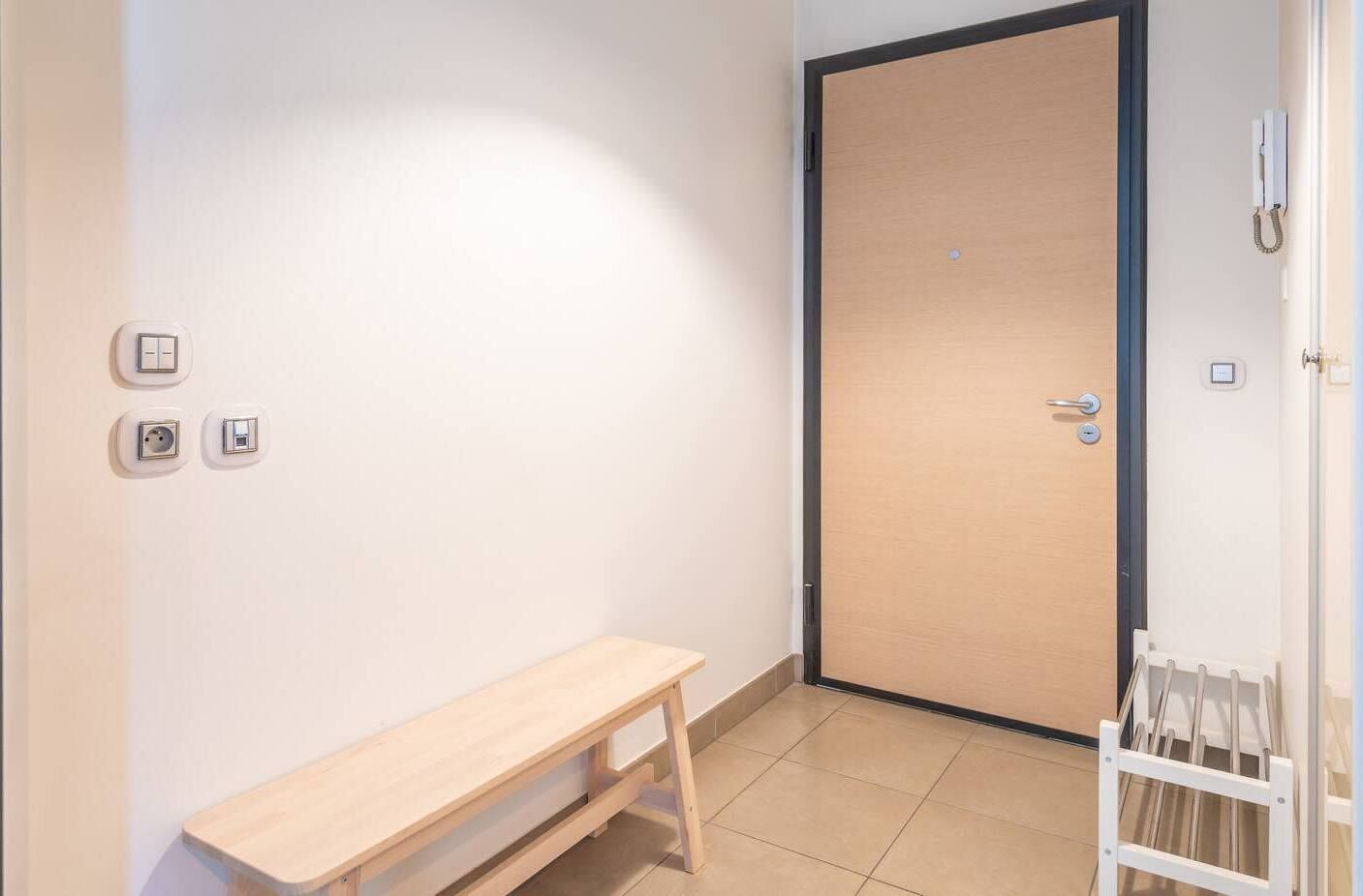 Une petite pièce propre, avec un banc en bois, une porte et un radiateur.