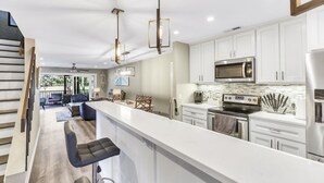 A modern kitchen with white cabinets, stainless steel appliances, and a bar area with stools.