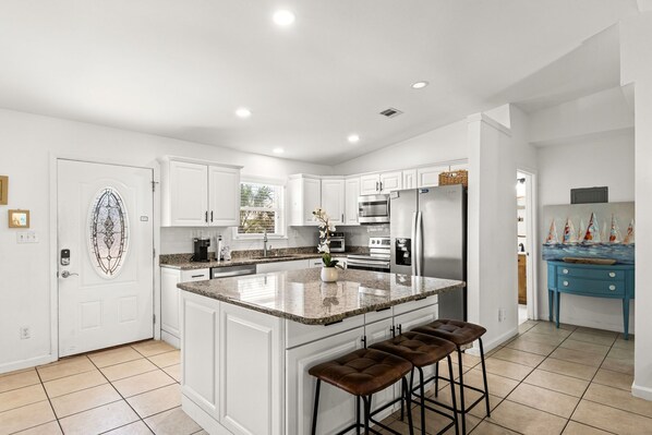 A modern kitchen with white cabinetry, a granite island, and a blue accent wall.