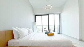 A modern hotel room with a large bed, a view of the city through floor-to-ceiling windows, and a balcony with outdoor seating.
