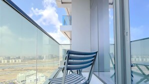 A balcony with a chair, glass railings, and a view of buildings and roads.