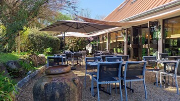 Un patio al aire libre con mesas y sillas, un paraguas grande y un hogar rústico.