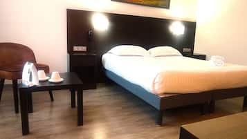 A hotel room with a bed, bedside table, chair, and a painting on the wall.