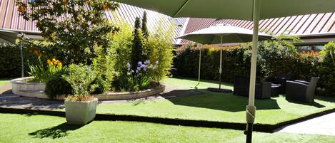 A patio area with a green lawn, outdoor furniture, and a large umbrella.