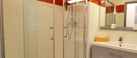 A modern bathroom with a glass-enclosed shower, white and red tiled walls, a white sink with a mirror, and a wooden tissue box.