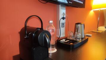 A hotel room with a television displaying a menu, a coffee maker, a water bottle, and a pair of headphones on a wooden table.