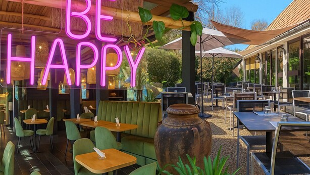An outdoor dining area with green seating, a neon sign reading "BE HAPPY", and a rustic pot in the foreground. - Contact Hotel B&G (Limoges)