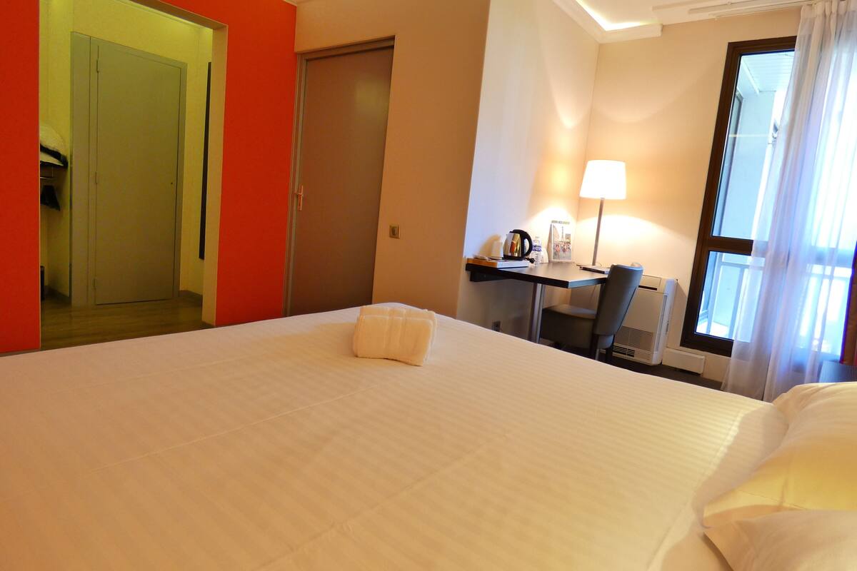 A hotel room with a large bed, a desk with a lamp, and a window with curtains.