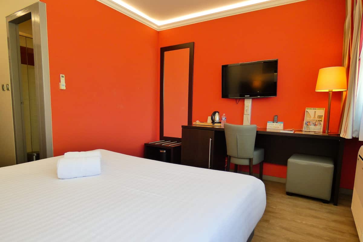 A hotel room with a bed, desk, chair, television, and a small trash bin.