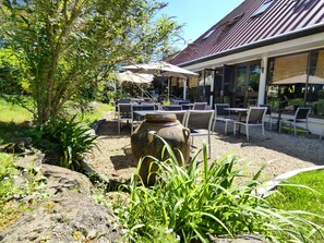 An outdoor seating area with tables and chairs, a large decorative pot, and a building with a sloped roof. - Contact Hotel B&G (Limoges)