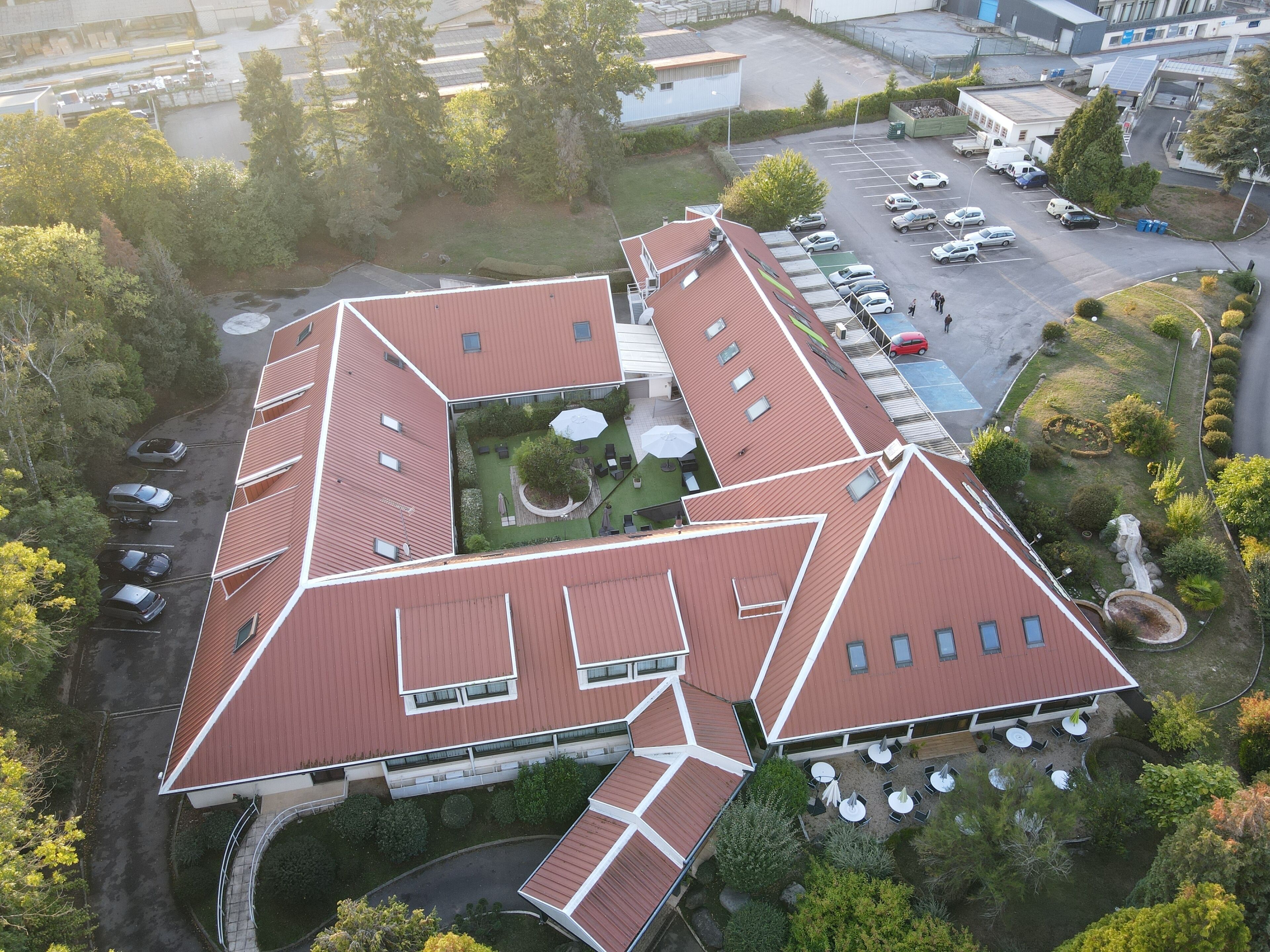 An aerial view of a building with a unique geometric roof design, multiple parking spaces, and outdoor seating areas.