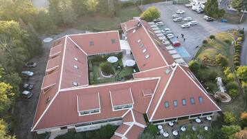 An aerial view of a building with a unique geometric roof design, multiple parking spaces, and outdoor seating areas.