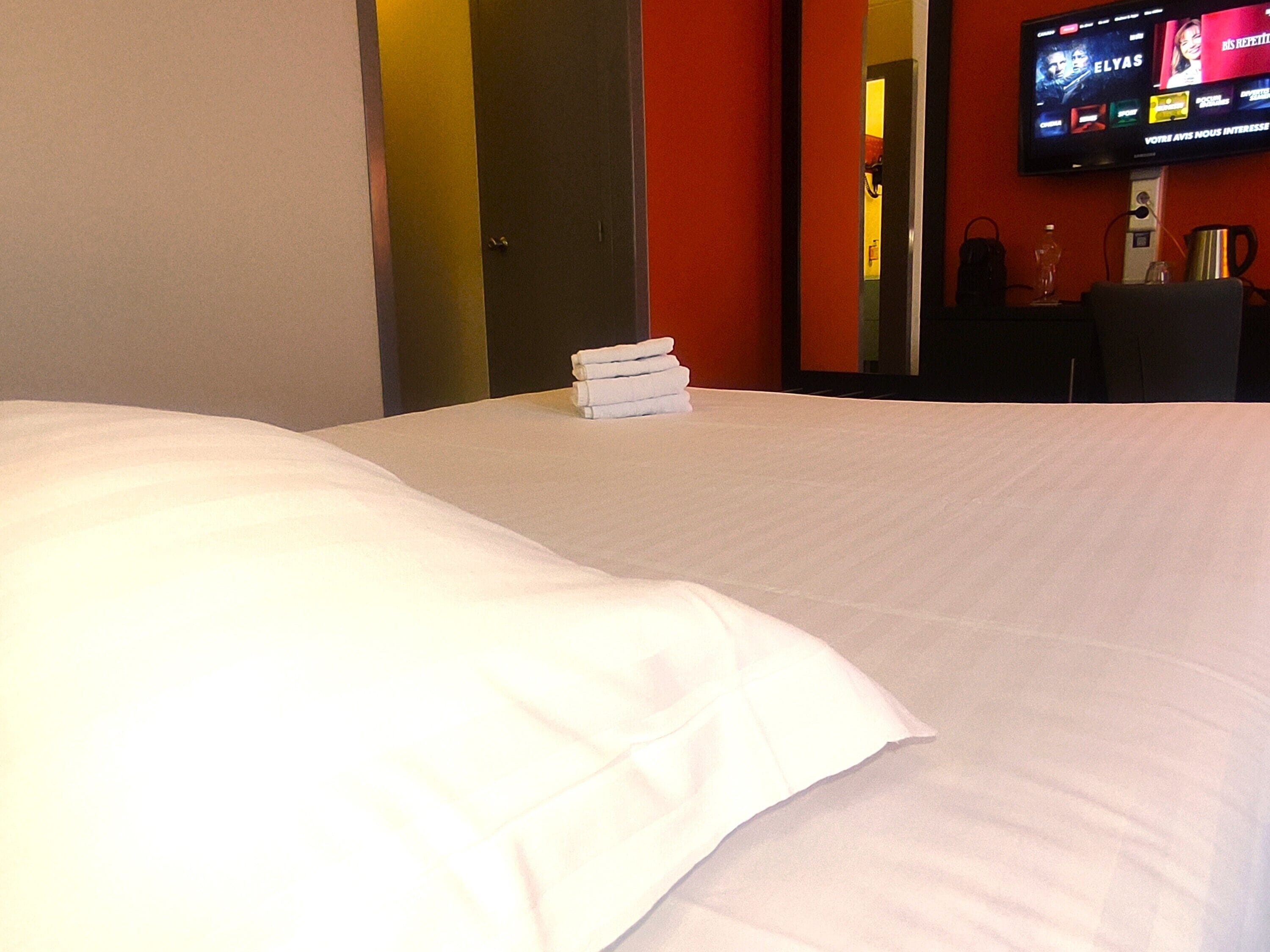 A hotel room with a neatly made bed, a television mounted on the wall, and a door leading to another room.