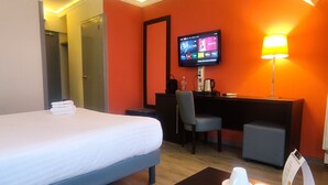 A hotel room with a bed, a desk, a chair, a TV, a lamp, and a coffee table with cups and saucers. - Contact Hotel B&G (Limoges)