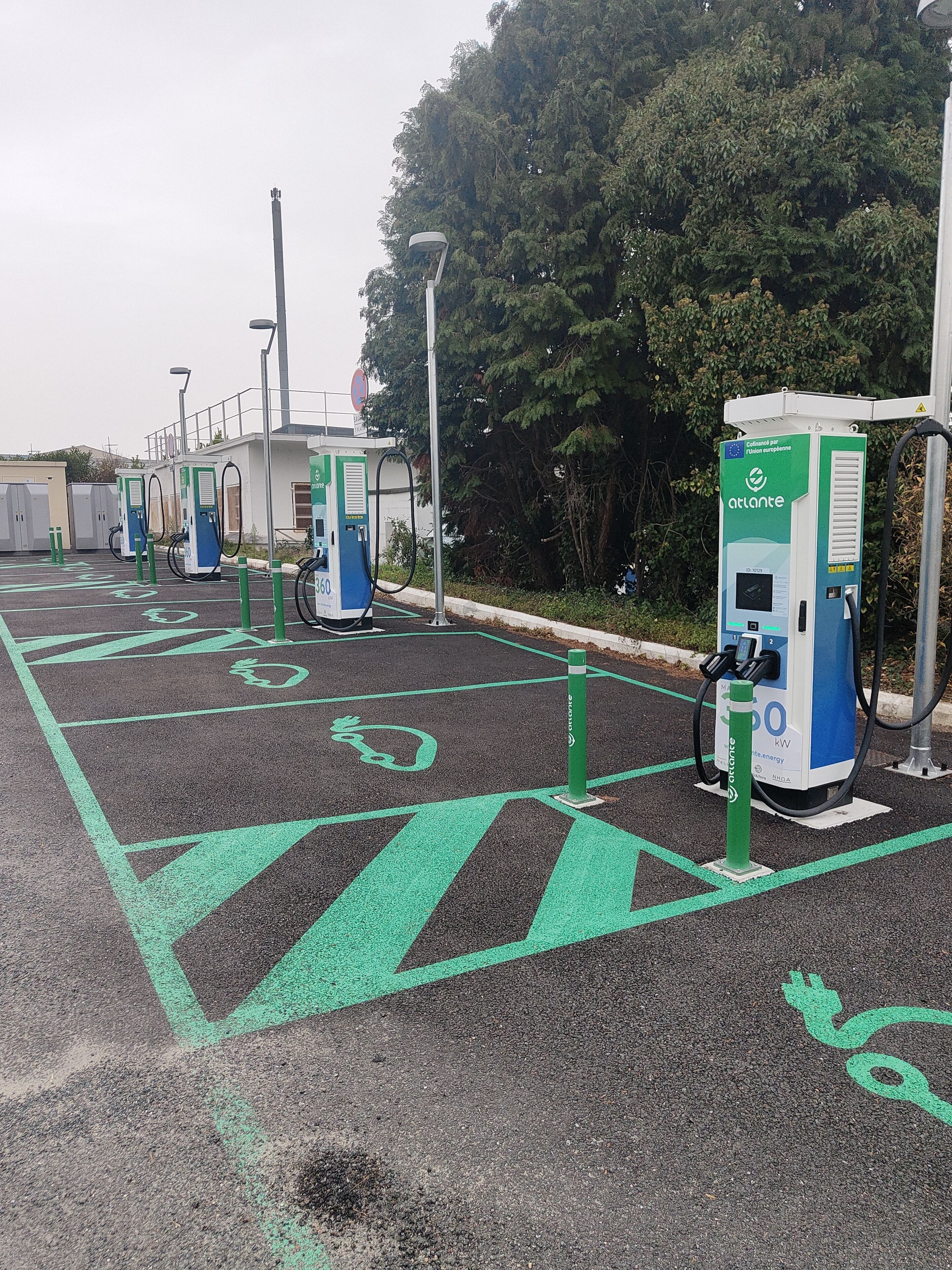 A parking area with electric vehicle charging stations, marked parking spaces, and a building in the background.
