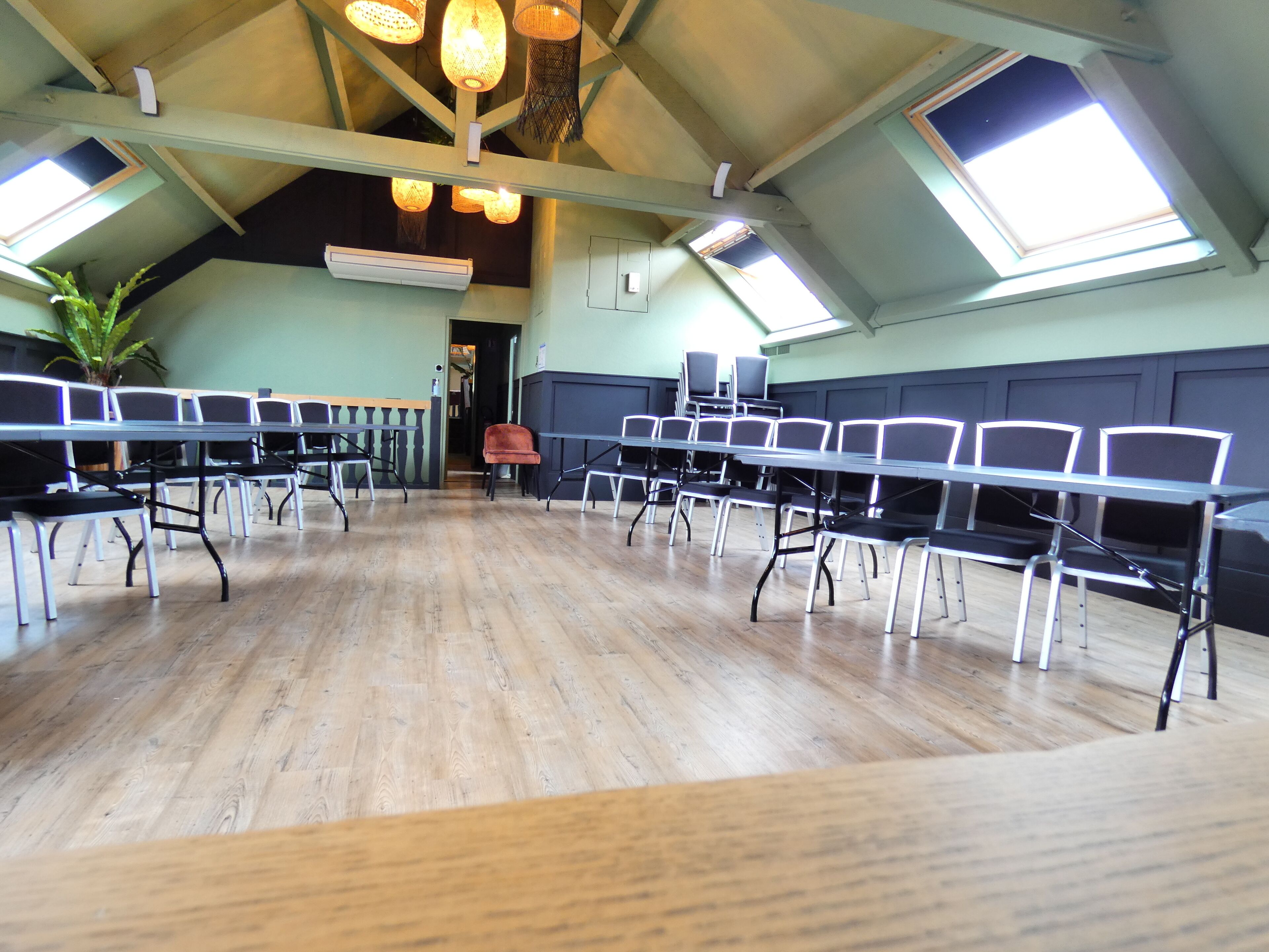 Un salón de conferencias con techos altos, tragaluces y suelo de madera. Mesas y sillas dispuestas para reuniones.