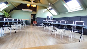 A conference room with high ceilings, skylights, and a wooden floor. Tables and chairs are arranged for meetings.