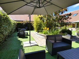 Un patio con mobiliario exterior, una pérgola y un jardín con plantas y un pequeño estanque.