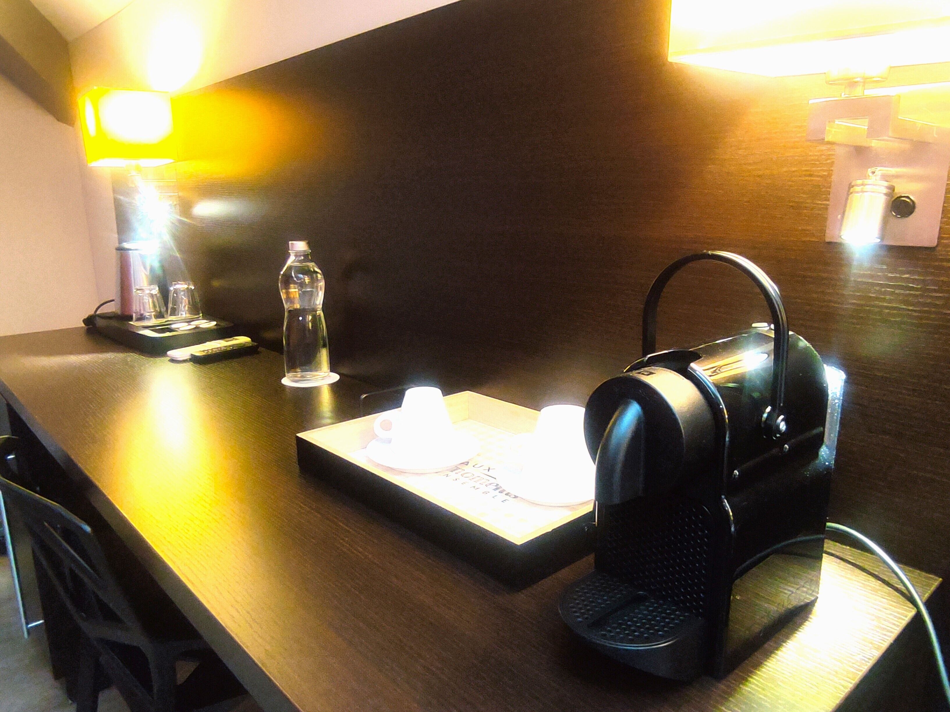 A hotel room counter with a coffee maker, a water bottle, and a remote control.