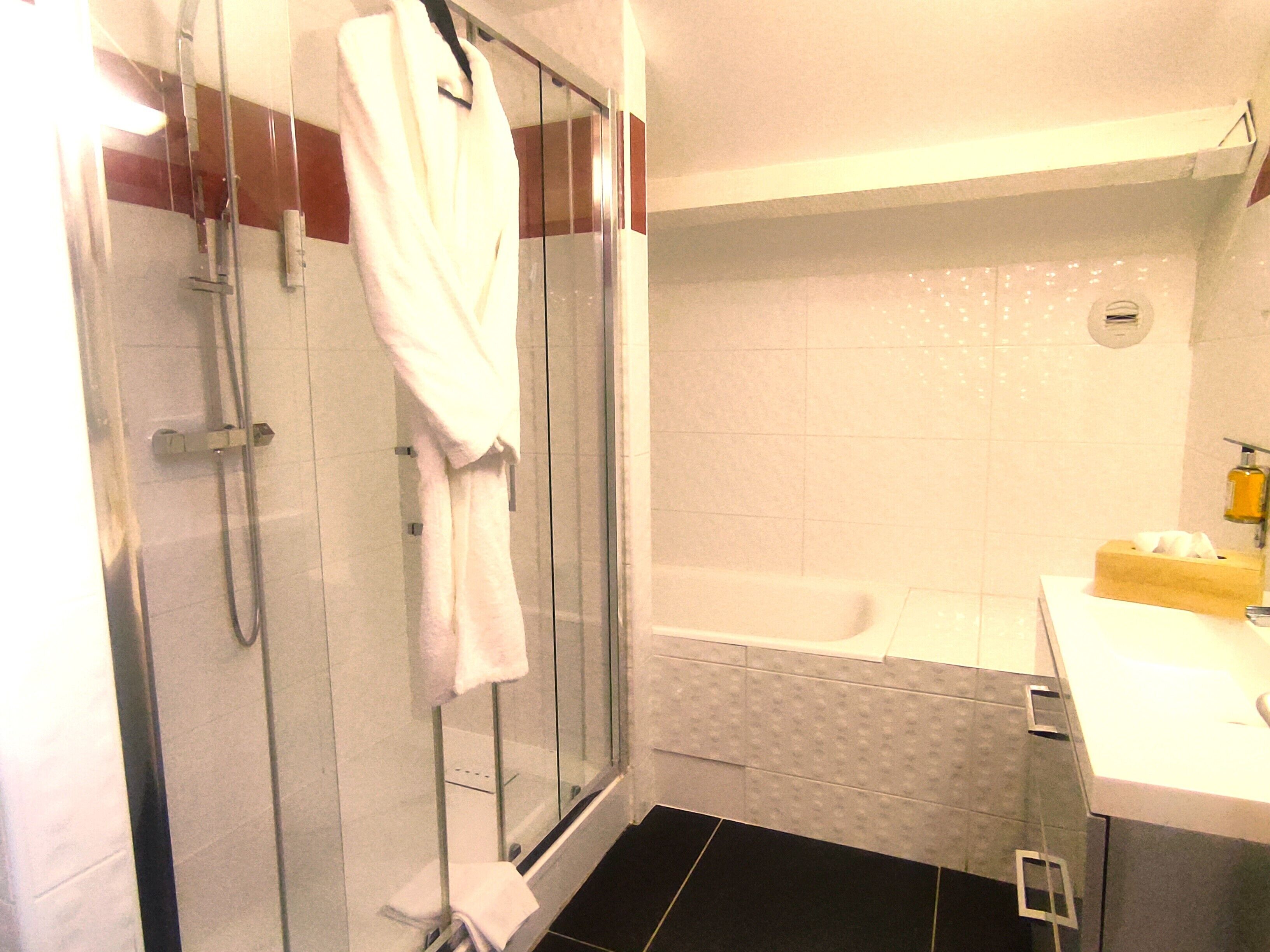 A bathroom with a glass shower enclosure, a white bathtub, and a sink with a soap dispenser.