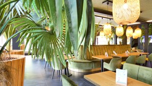 A restaurant interior with green upholstered seating, wooden tables, and hanging wicker lamps. - Contact Hotel B&G (Limoges)