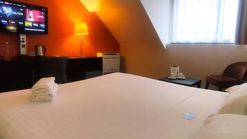 A hotel room with a large bed, a desk with a lamp, a television on the wall, and a window with curtains.