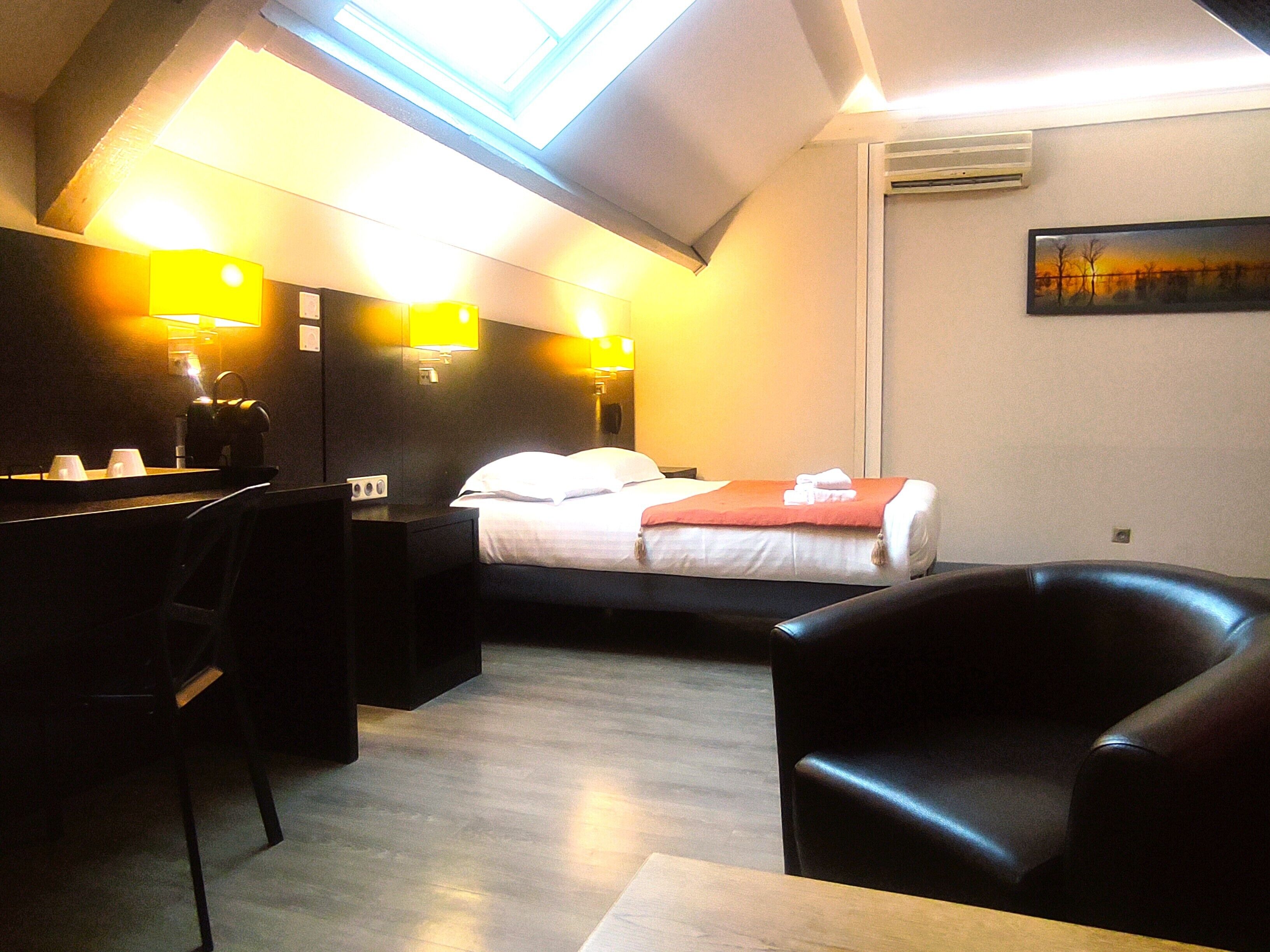 A hotel room with a bed, a desk, a chair, and a skylight.