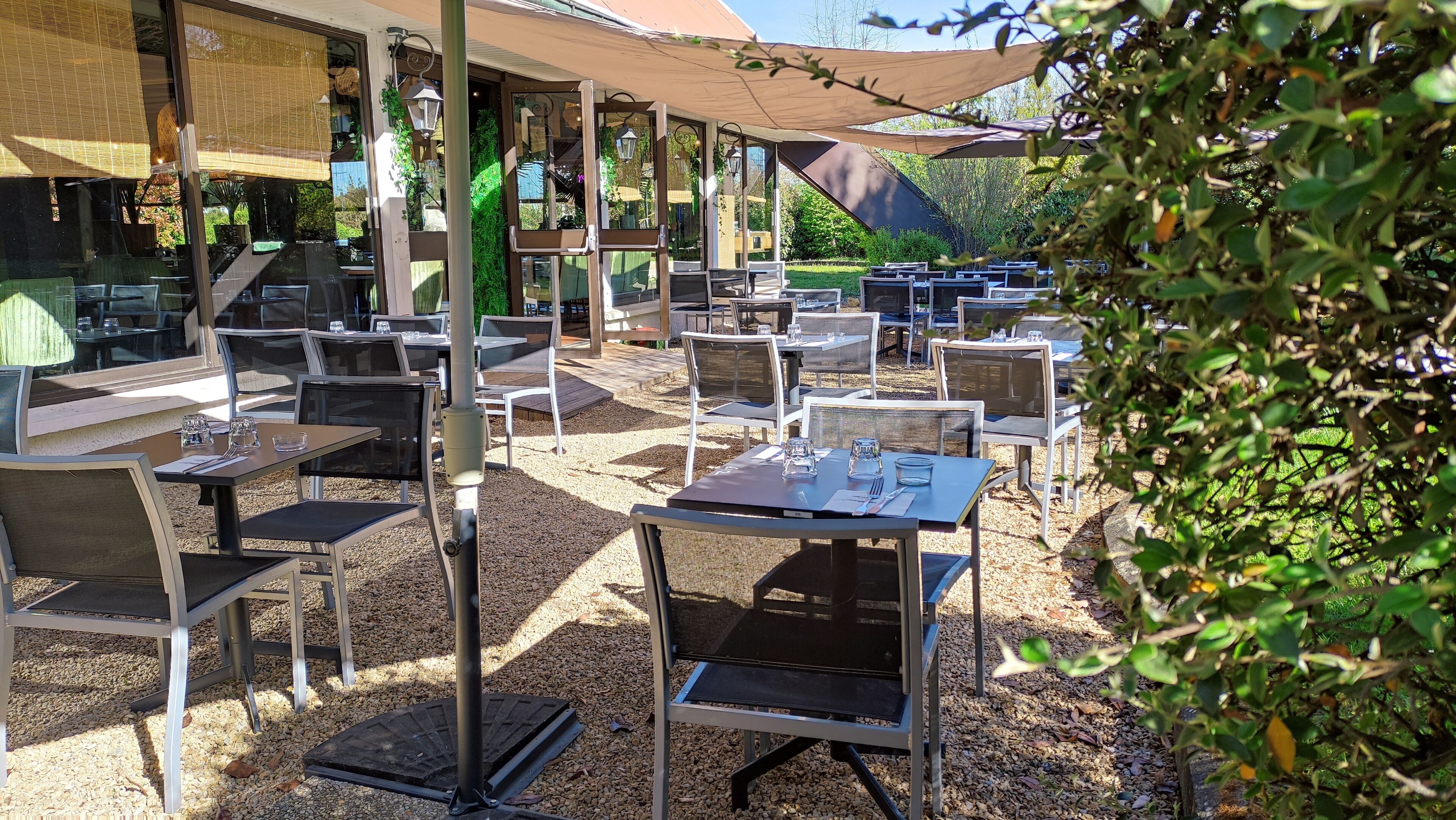 Un espace extérieur aménagé avec des tables et des chaises, protégé par des parasols et entouré de verdure.