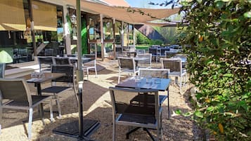 Un espace extérieur aménagé avec des tables et des chaises, protégé par des parasols et entouré de verdure.