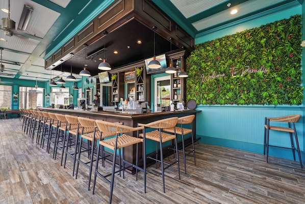 Un espace bar doté d’un long comptoir, de tabourets de bar et d’un mur vert orné d’une enseigne.