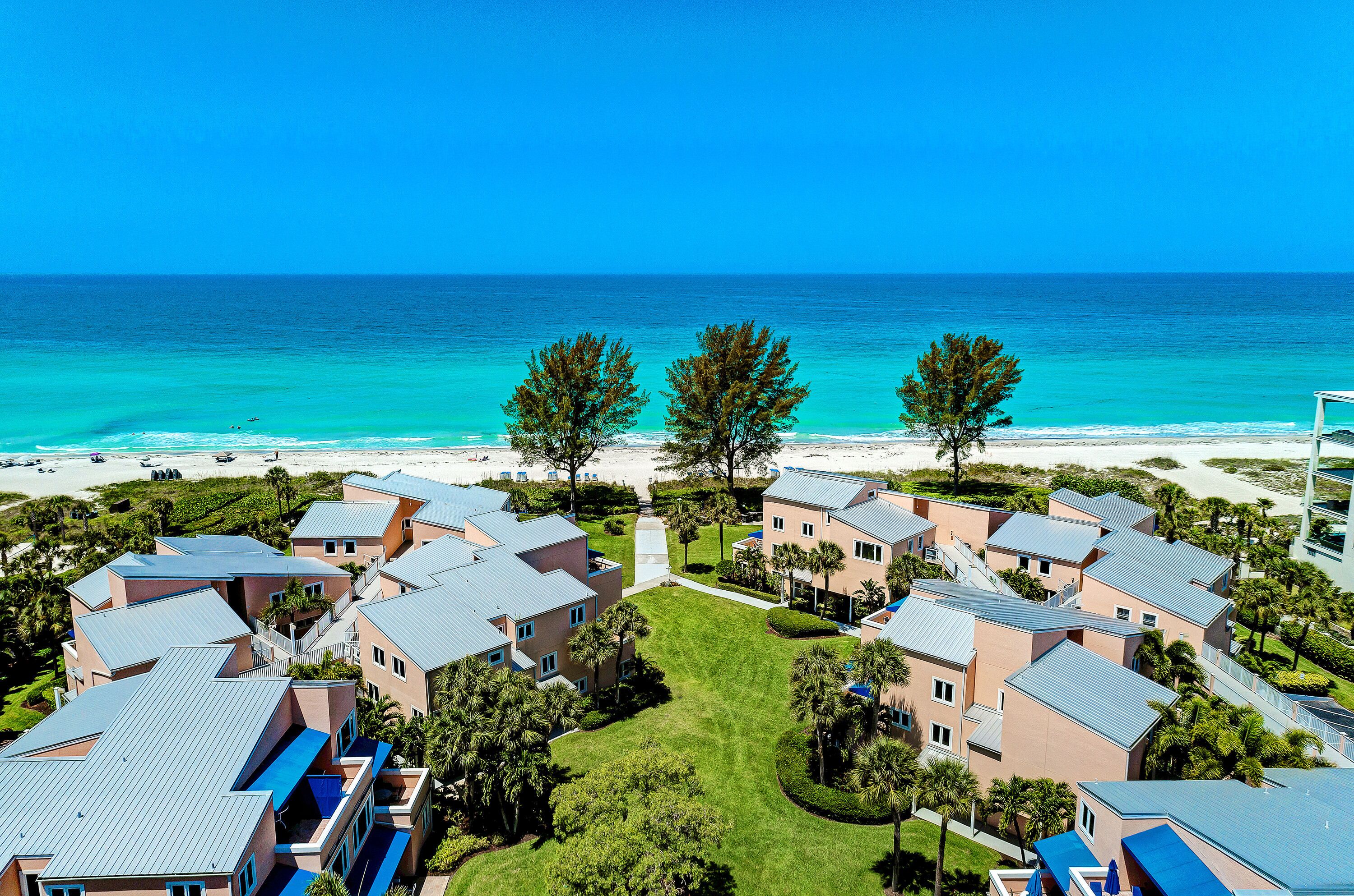 Un complexe hôtelier comprenant plusieurs bâtiments, une plage et un ciel d’un bleu limpide.