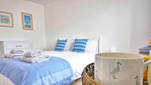 Ein ordentlich bezogenes Bett mit blau-weißer Bettwäsche, eine weiße Tasse mit Entenmotiv und ein Korbwäschekörbchen.