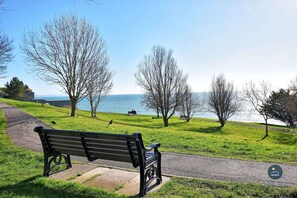 A park bench facing a body of water with trees and a clear sky. - Capstan Cottage - harbour cottage with parking (Weymouth)