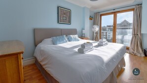 Een hotelkamer met een groot bed, een houten nachtkastje, een ingelijst schilderij aan de muur en een raam met gordijnen.